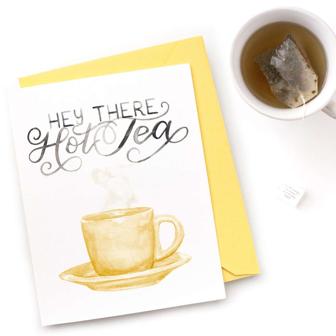 Image of a hand-lettered watercolor card saying "Hey There Hot Tea" with a painting of a tea cup and saucer by CharmCat | charmcat.net
