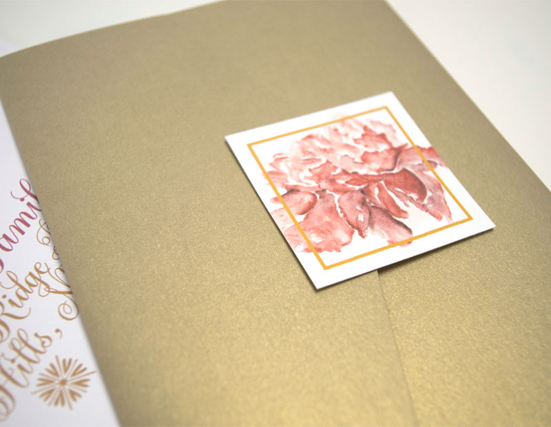 A gold pocketfold sealed with a square tag featuring a red peony design.